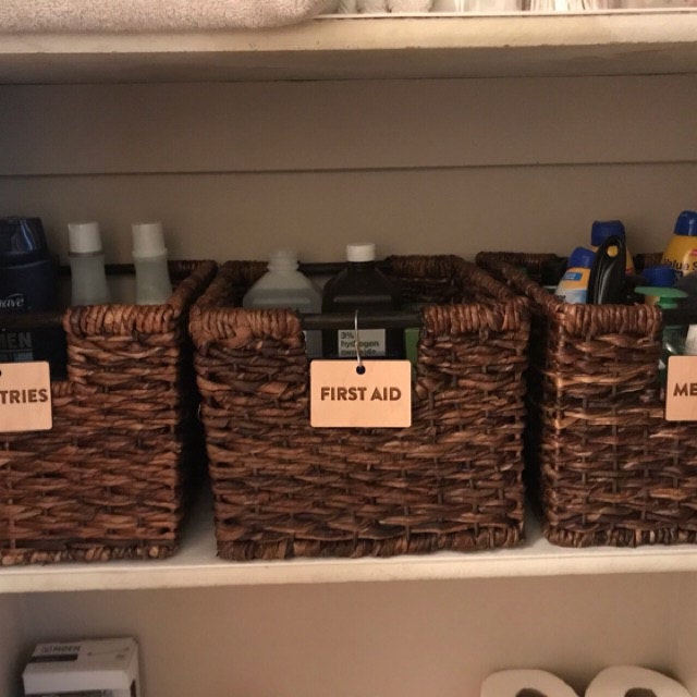 Hooked Labels for Storage Bin Organization - Maple Wood First Aid Clean Font hanging from wicker baskets - by LeeMo Designs in Bend, Oregon